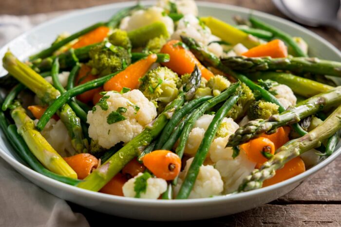 Para unosi się z bambusowego koszyka parowego pełnego świeżych warzyw i ryby